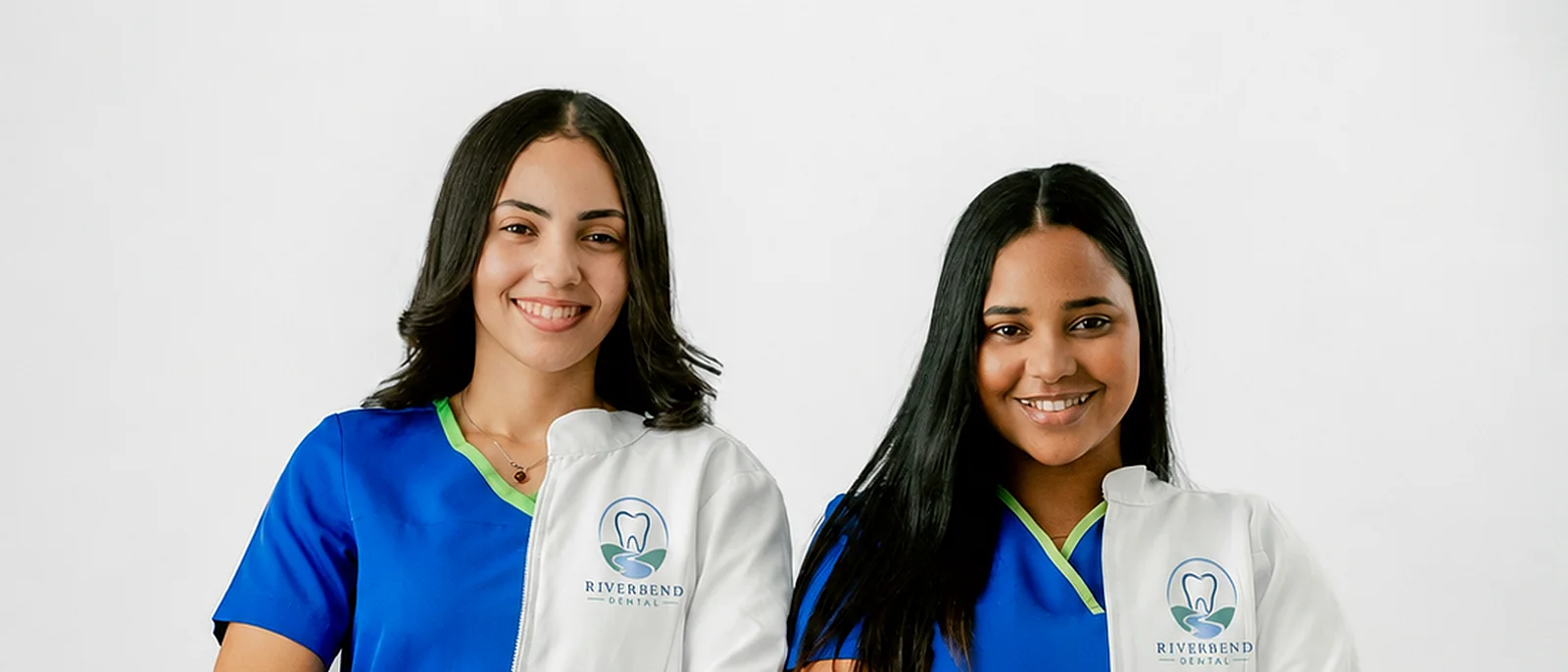 Two Riverbend Dental team members in branded scrubs and lab coats